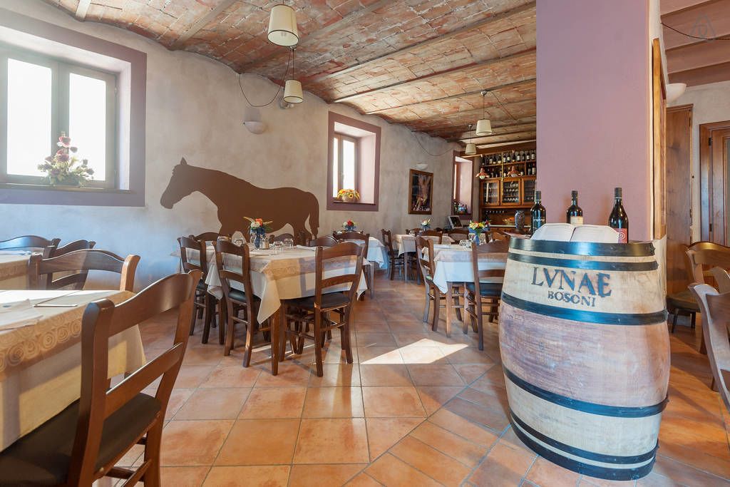 A rustic dining area with wooden tables and chairs, a large barrel labeled 'LVNAE BOSONI', and a wall mural of a horse.