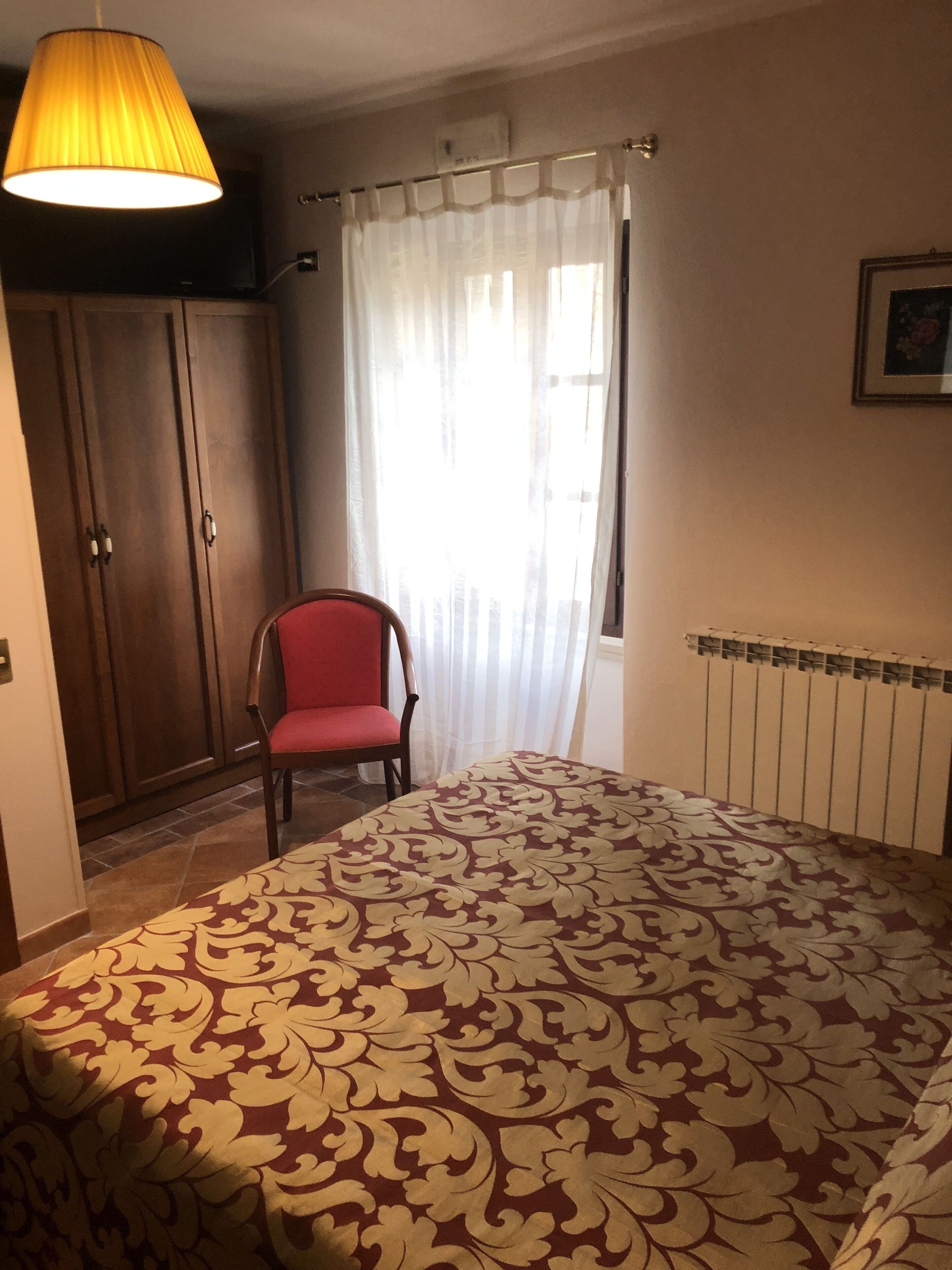 A bedroom with a bed, a chair, a wardrobe, a radiator, and a window with curtains.