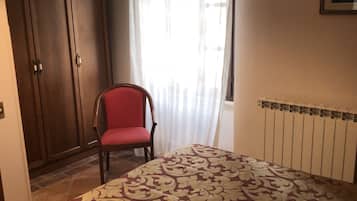 A bedroom with a bed, a chair, a wardrobe, a radiator, and a window with curtains.