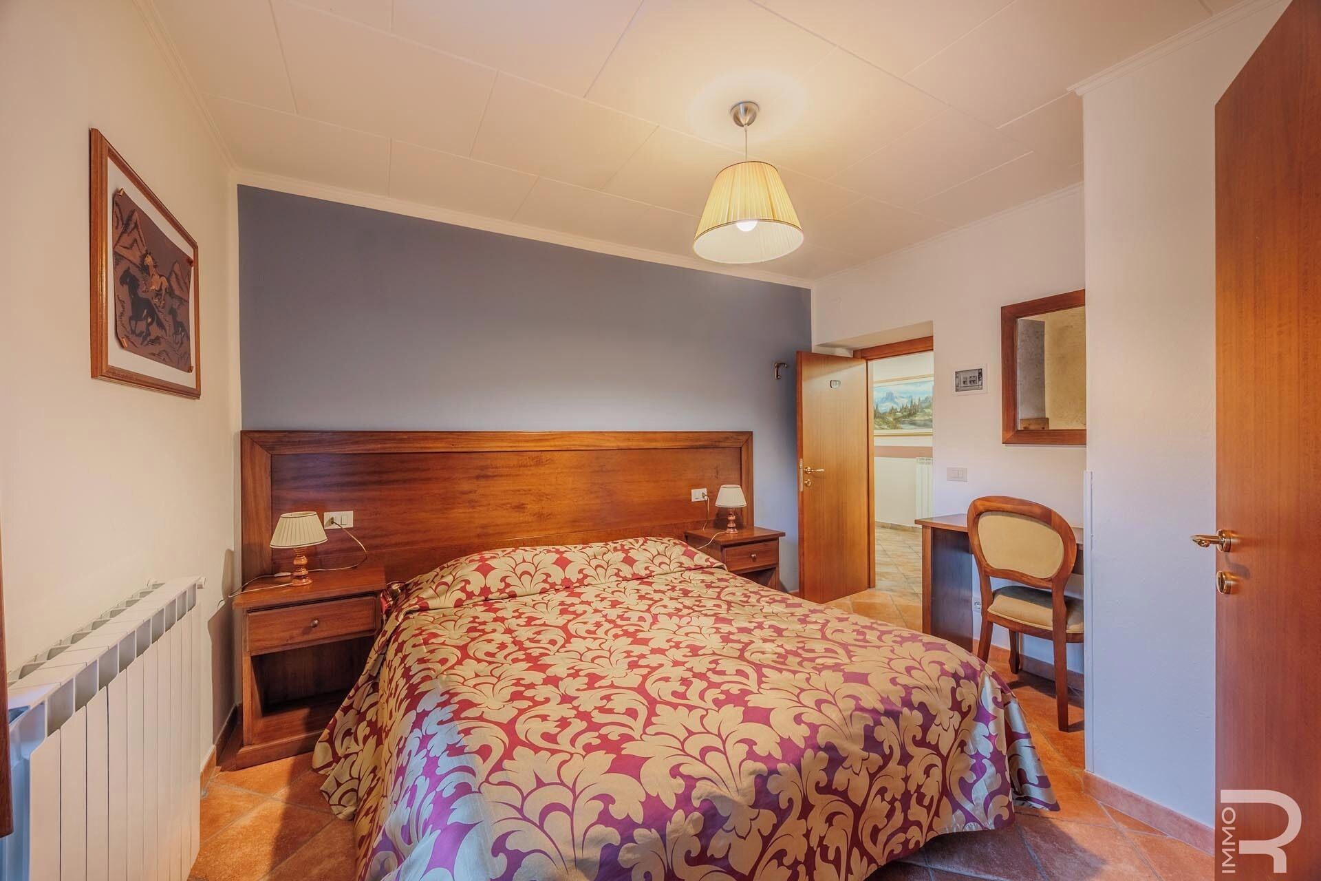 Une chambre à coucher avec une tête de lit en bois, une couvre-lit à motifs, une lampe de chevet et une porte donnant sur une autre pièce.
