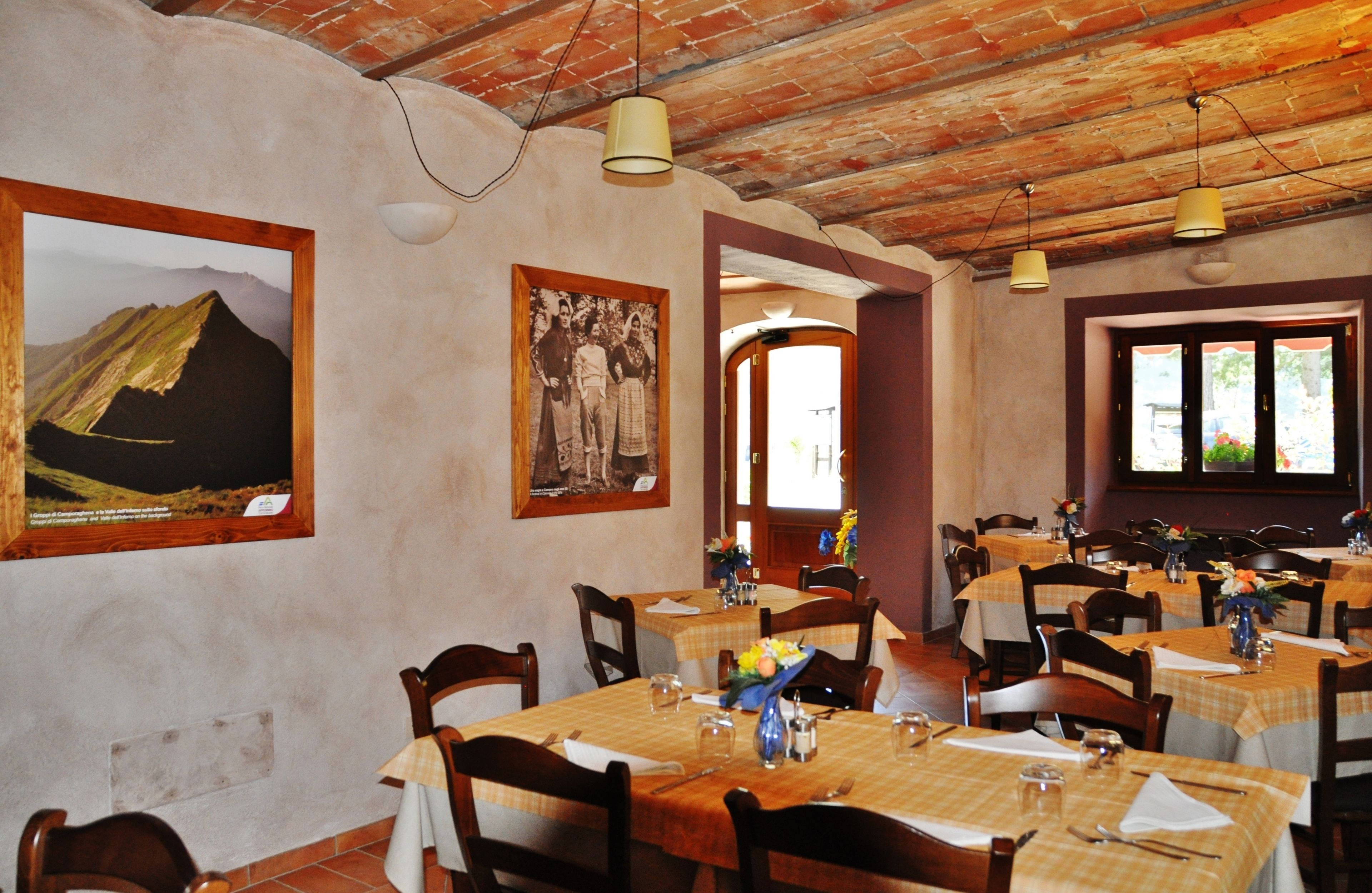 Un comedor con mesas dispuestas para comer, cuadros en las paredes y un techo rústico.
