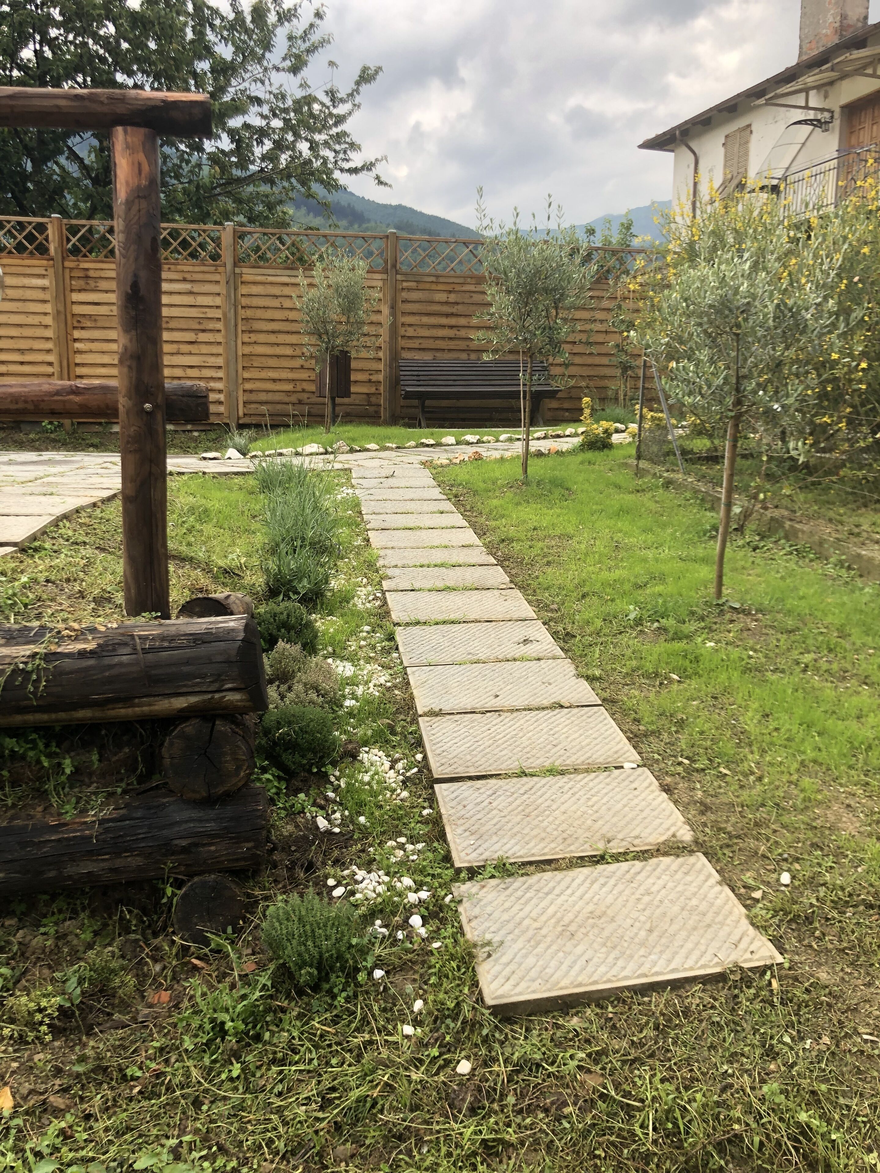 Un sendero en un jardín que lleva a un banco de madera y un edificio con valla de madera.