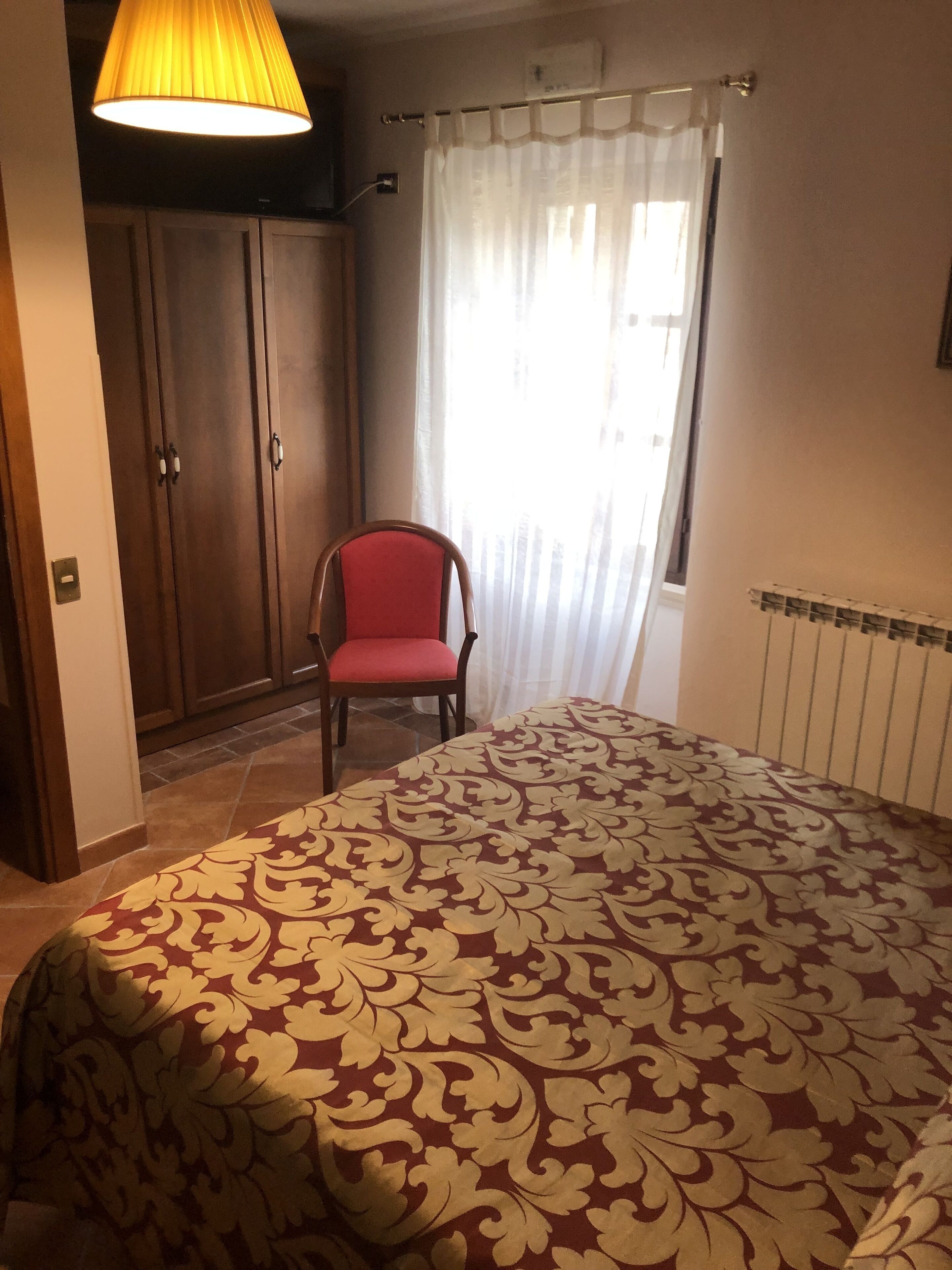 Een slaapkamer met een groot bed, een stoel, een kledingkast en een raam met gordijnen.