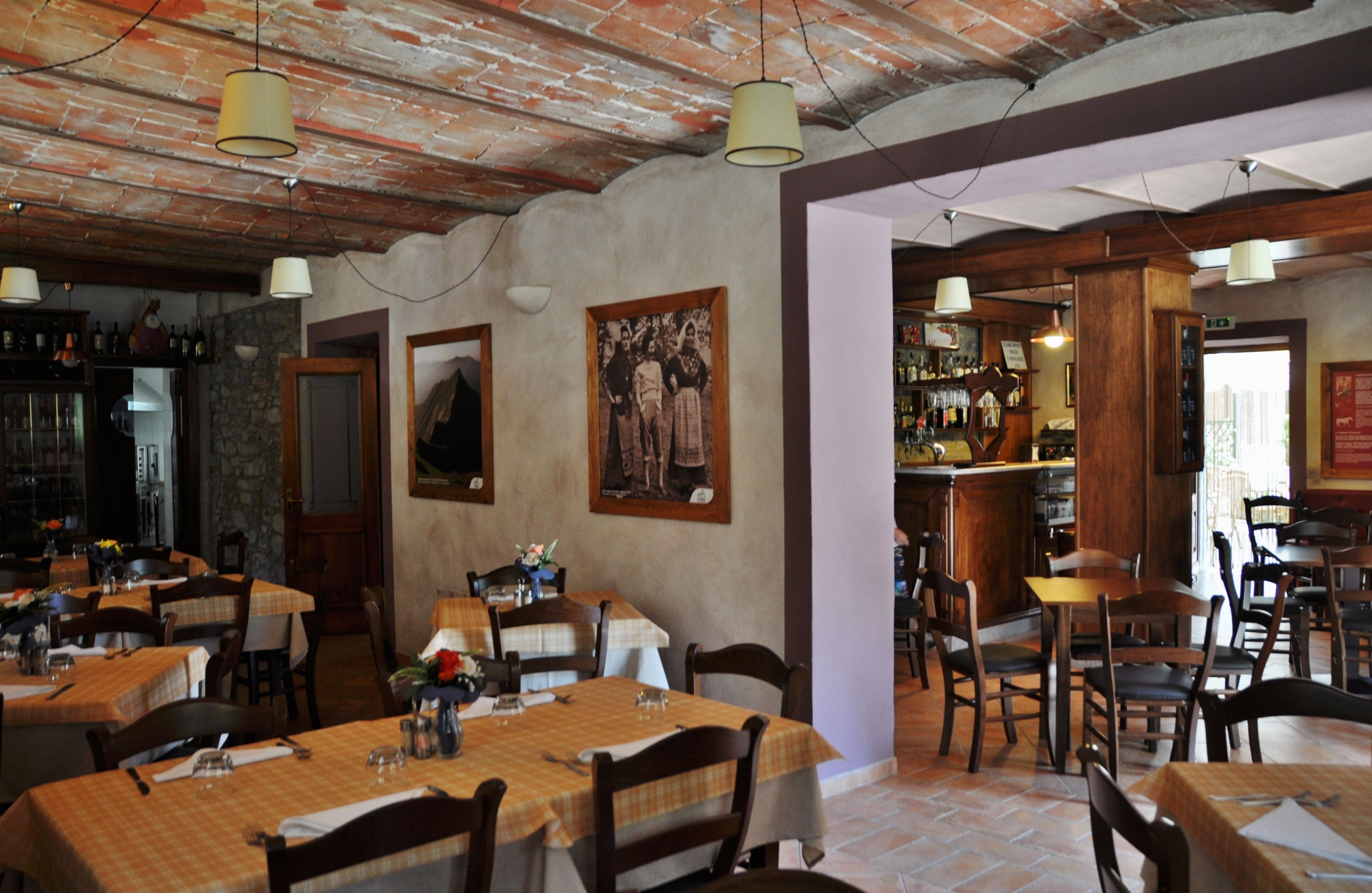 Un restaurante con mesas y sillas de madera, techo de ladrillo y lámparas colgantes.