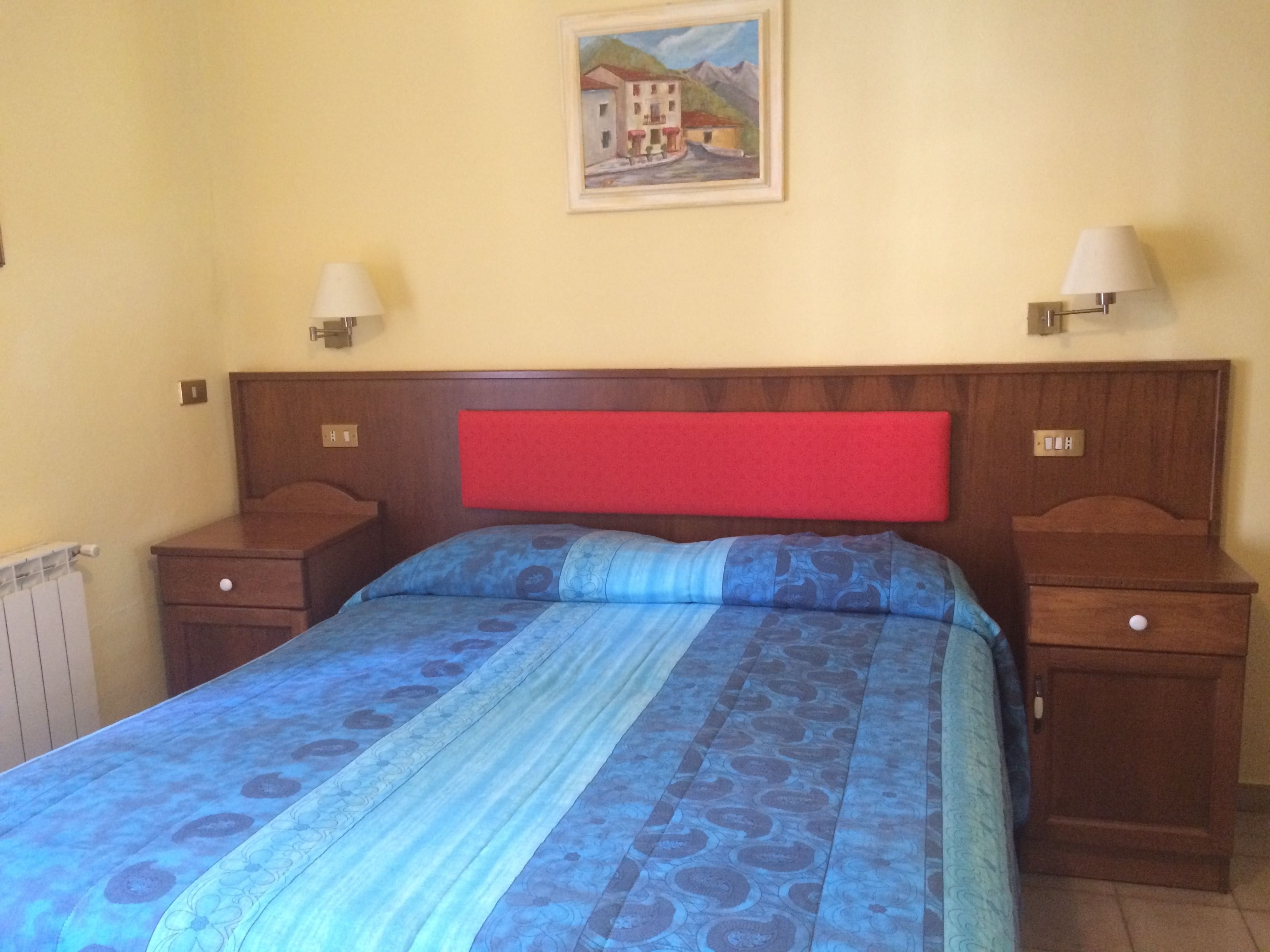 Una camera da letto con un letto, due comodini, una testiera rossa e un quadro appeso al muro.