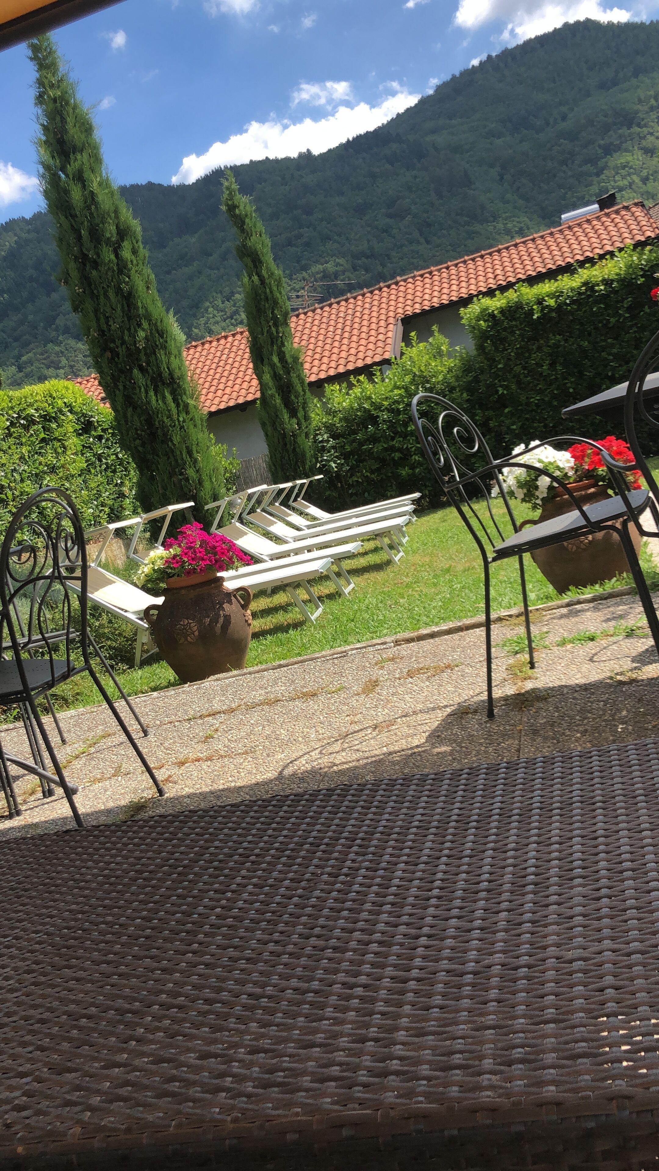 Eine Terrasse mit Gartenmöbeln, einem Blumentopf mit Blumen und Blick auf einen Berg sowie ein Gebäude mit Ziegeldach.