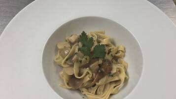 Two white plates of pasta with mushrooms and parsley on a stainless steel table.