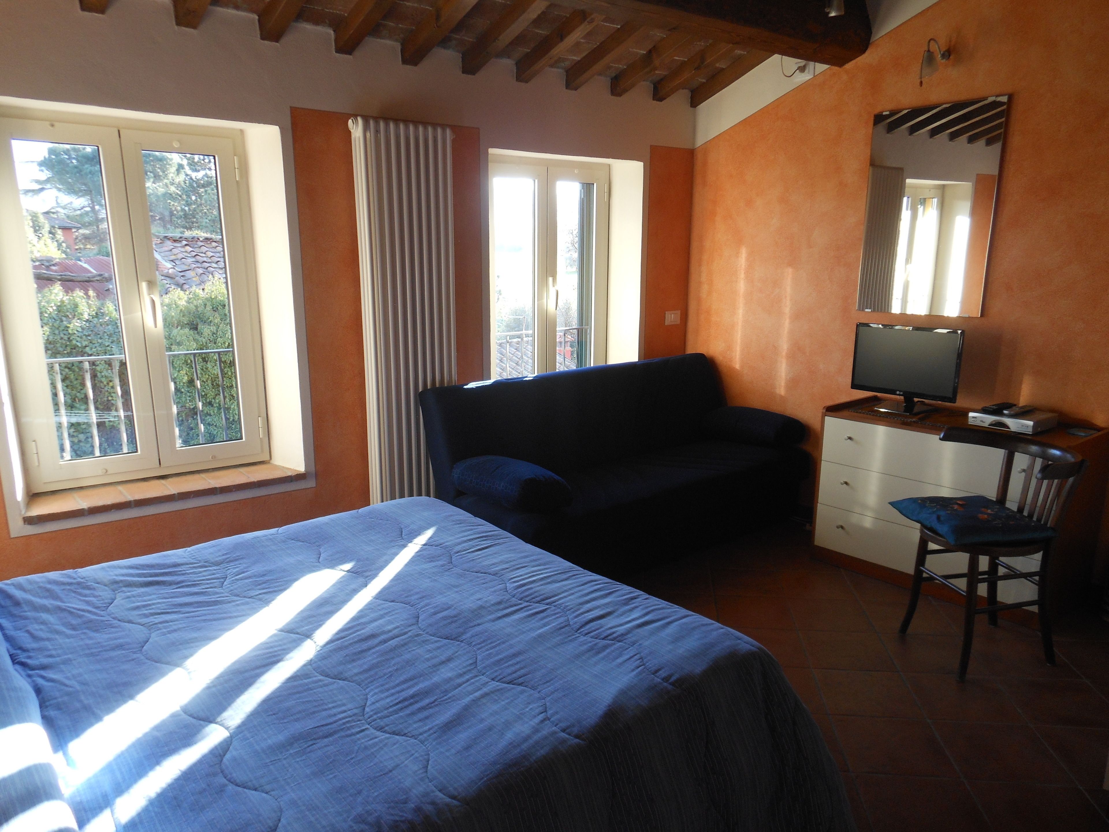 Un dormitorio con cama, una silla, escritorio, computadora y ventana con cortinas.