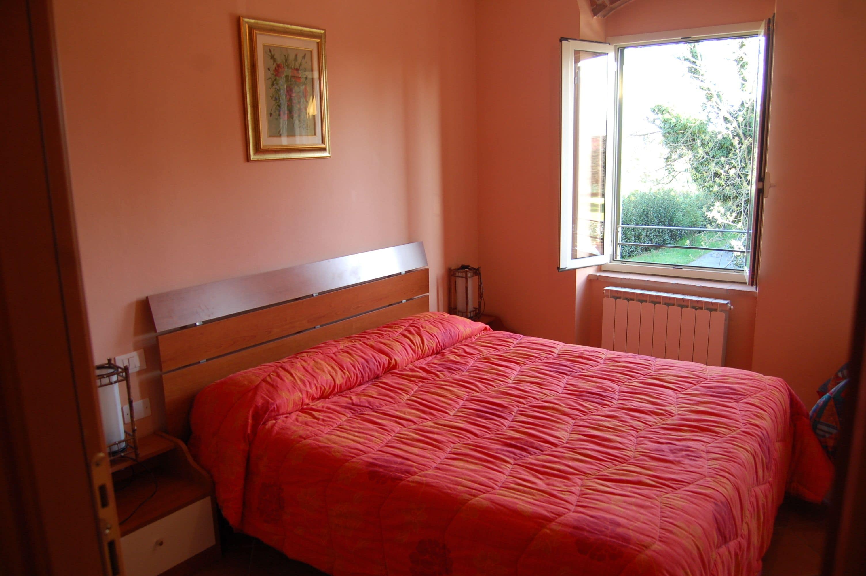 Une chambre à coucher avec un lit, un radiateur, une fenêtre et un tableau accroché au mur.
