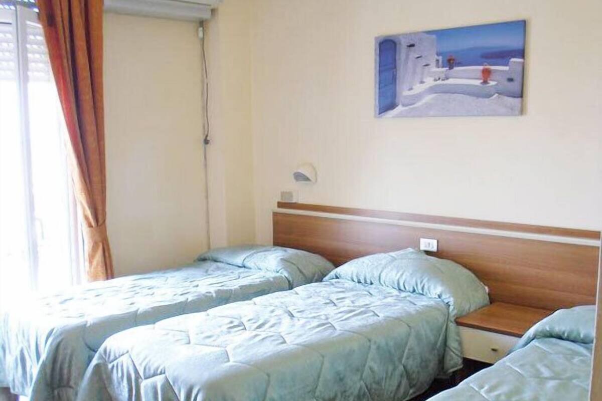 Een kamer met twee eenpersoonsbedden, een houten hoofdbord, een schilderij aan de muur en een raam met gordijnen.