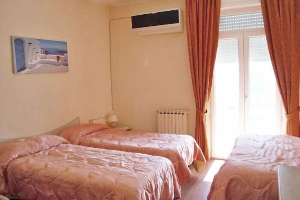 Een kamer met twee bedden, een radiator, een raam met gordijnen en een schilderij aan de muur.