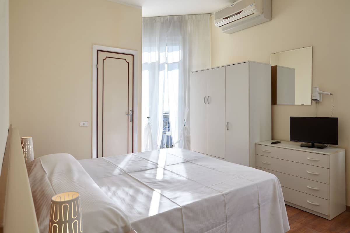 Een slaapkamer met een bed, een kledingkast, een televisie en een raam met gordijnen.