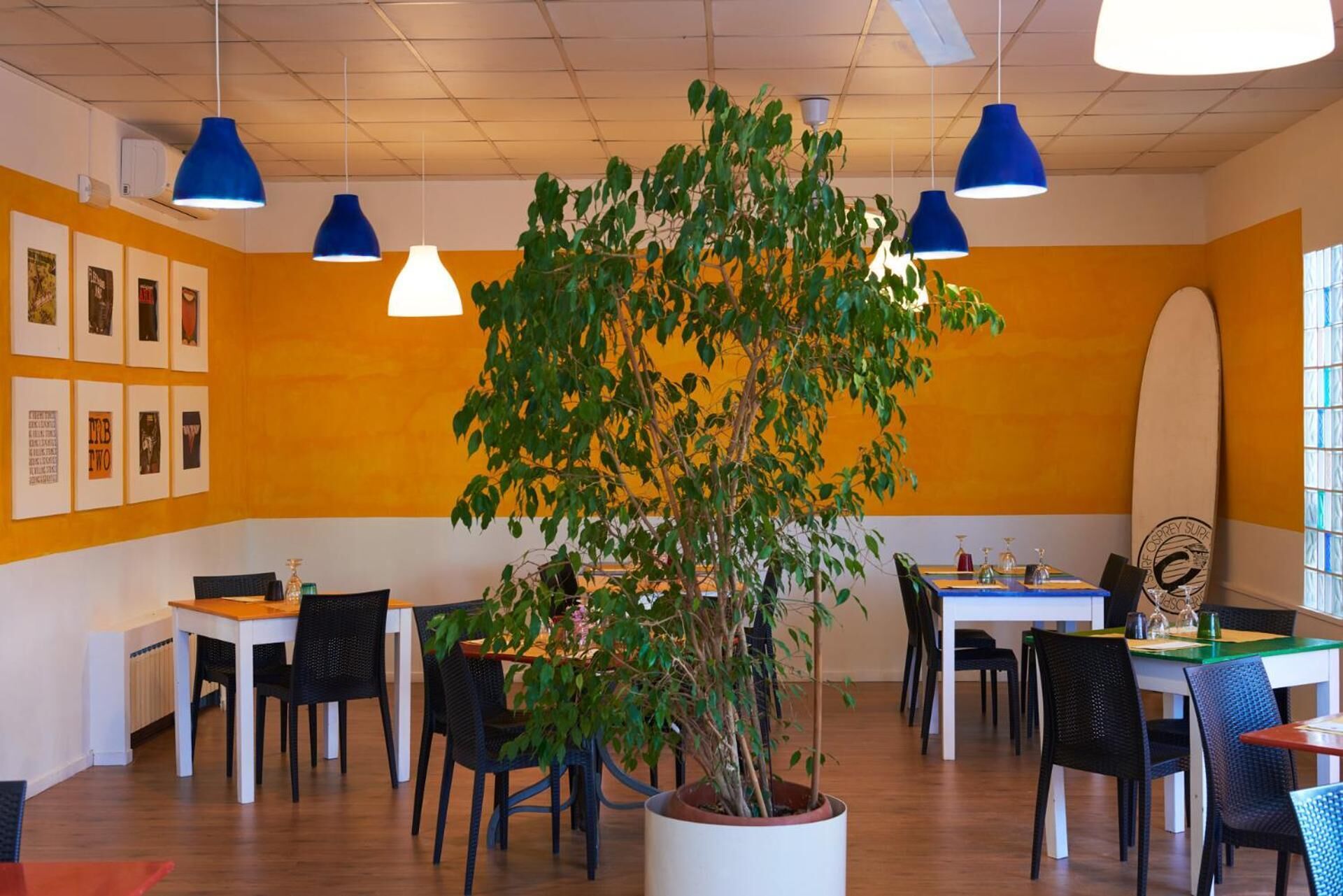 A restaurant with a central plant, tables, chairs, and blue pendant lights.