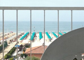 A beach view with rows of umbrellas and beach chairs, a clear sky, and the sea in the background.