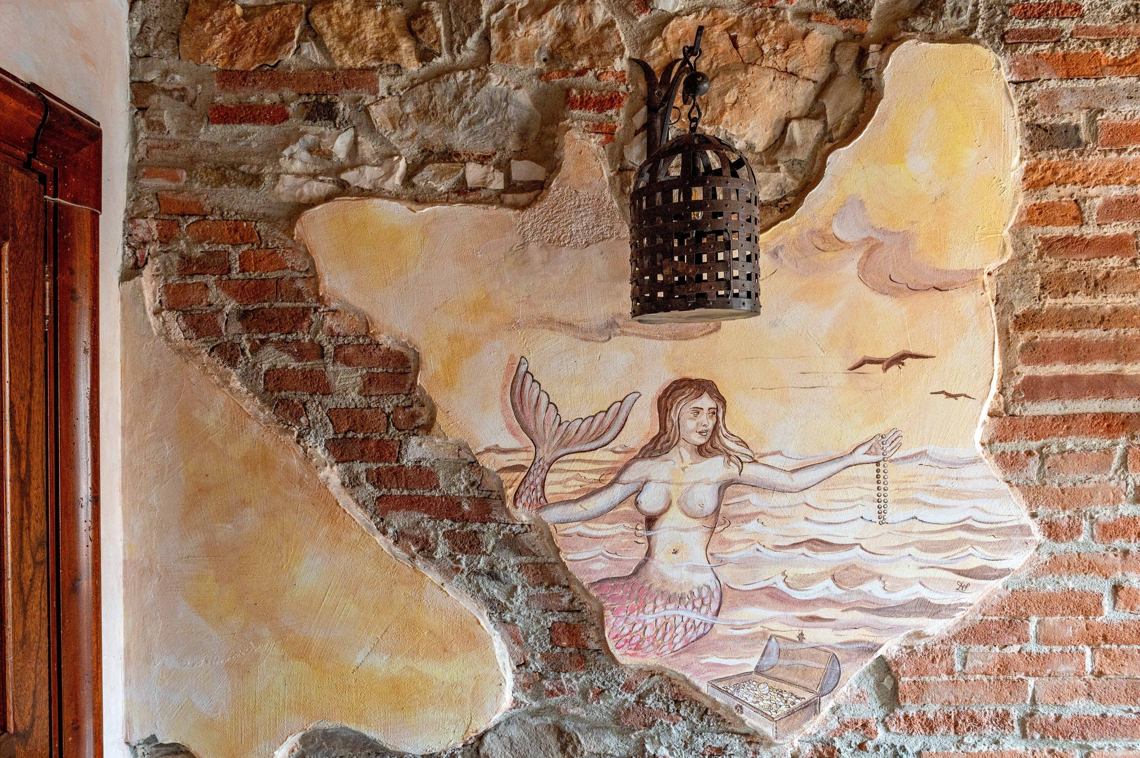 A mural of a mermaid with a lantern above her head, set against a brick wall.