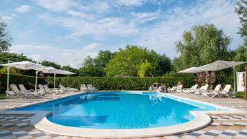 Una piscina con lettini e ombrelloni, immersa nel verde.