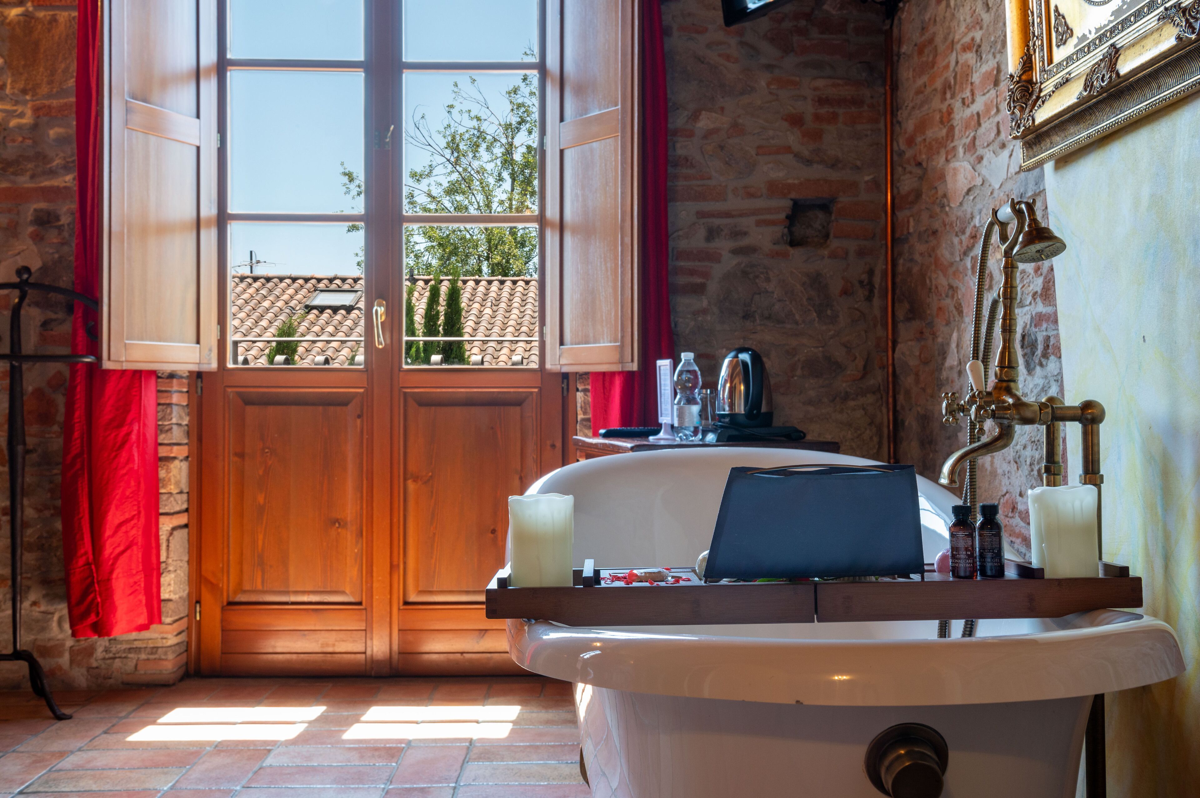 A bathroom with a bathtub, a wooden door, and a window with red curtains.