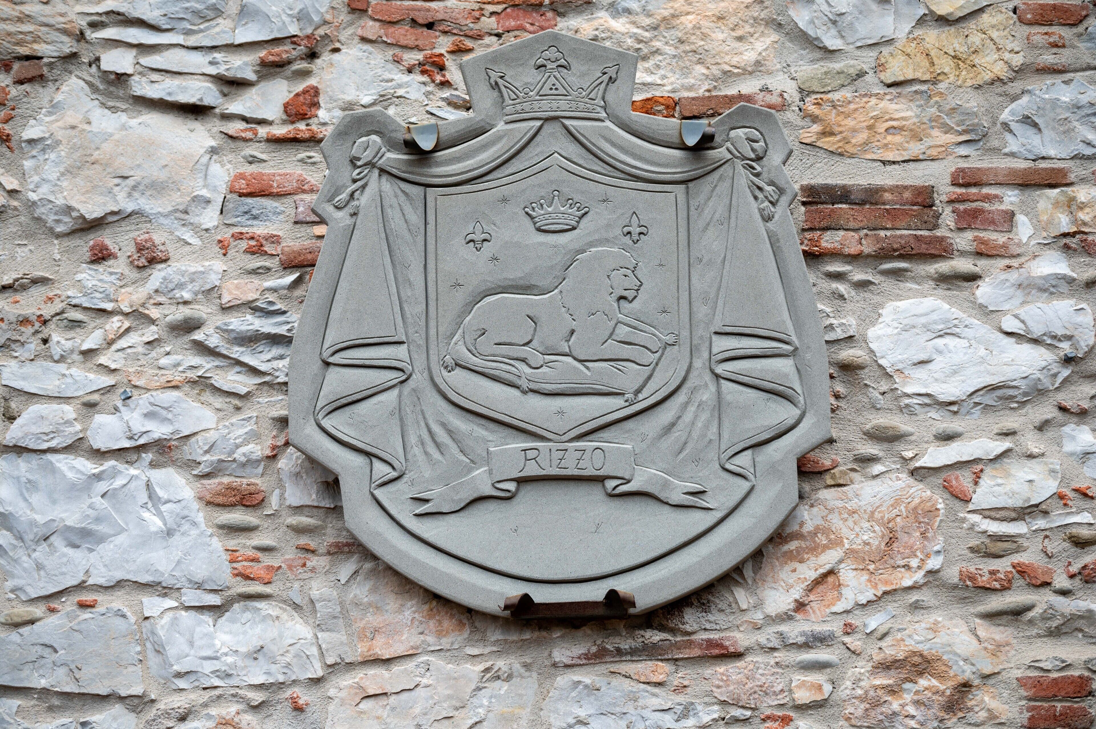 A stone coat of arms with a lion and the word "RIZZO" on a brick wall.
