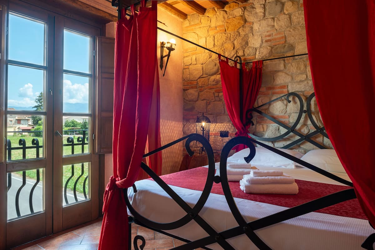 A bedroom with a stone wall, a bed with a metal frame, and a view through a glass door.