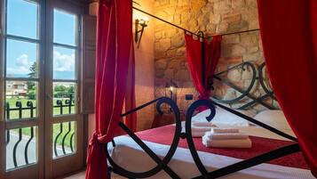 Un dormitorio con pared de piedra, cama con estructura metálica y vista a través de un ventanal.