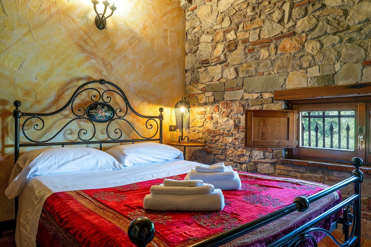 A bed with white linens, a red bedspread, and neatly folded towels.