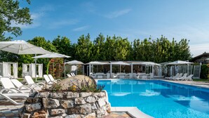 A swimming pool with lounge chairs and umbrellas, surrounded by a stone wall and greenery. - Villa Corte Degli Dei (Lucca)