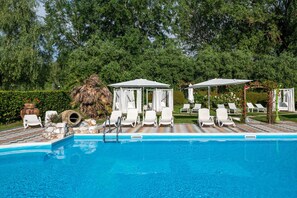 Un área de piscina con sillas de descanso, sombrillas y una estructura de piedra.