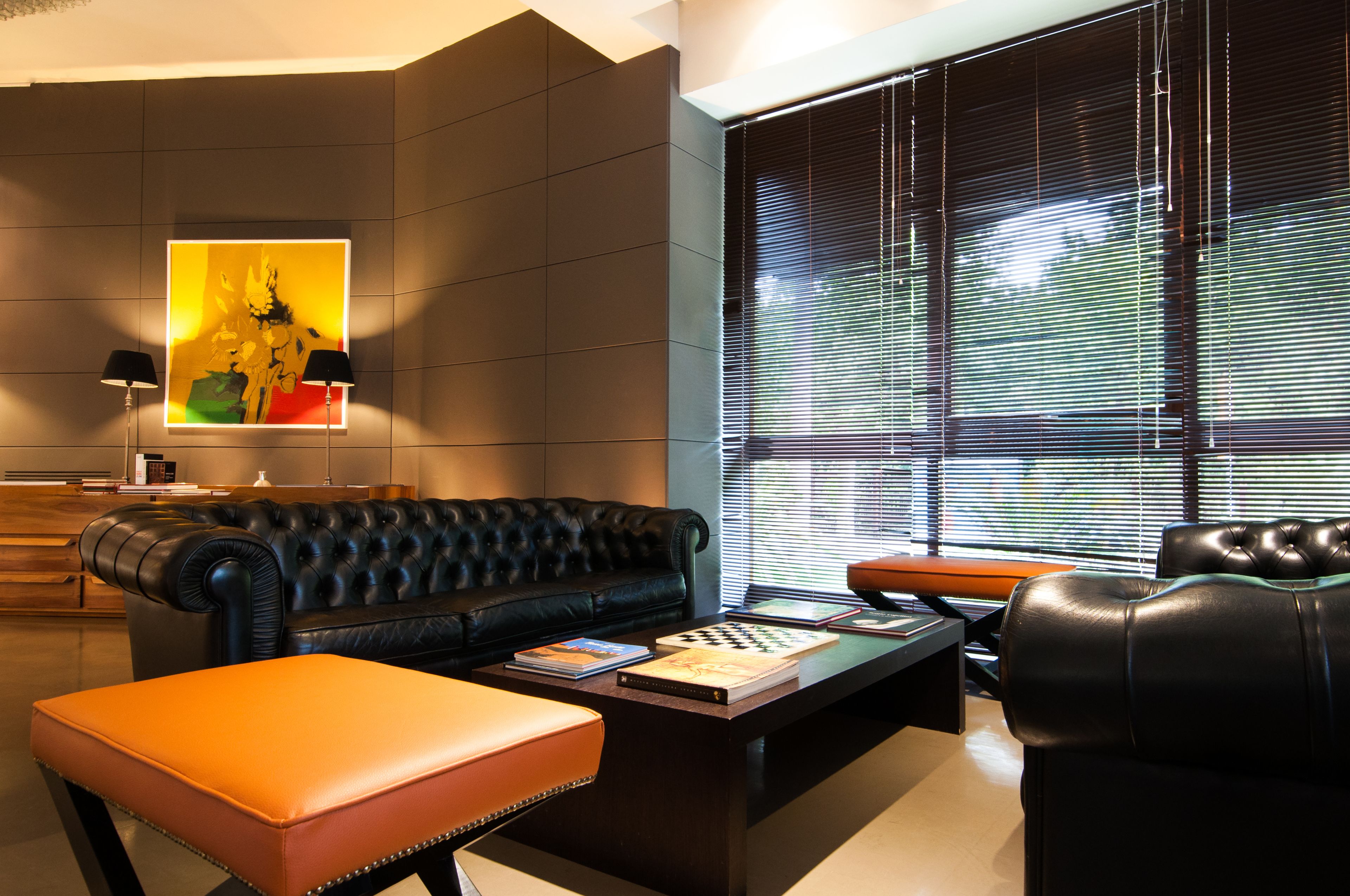 A modern living room with a black leather sofa, an orange ottoman, and a coffee table with books and a chessboard.