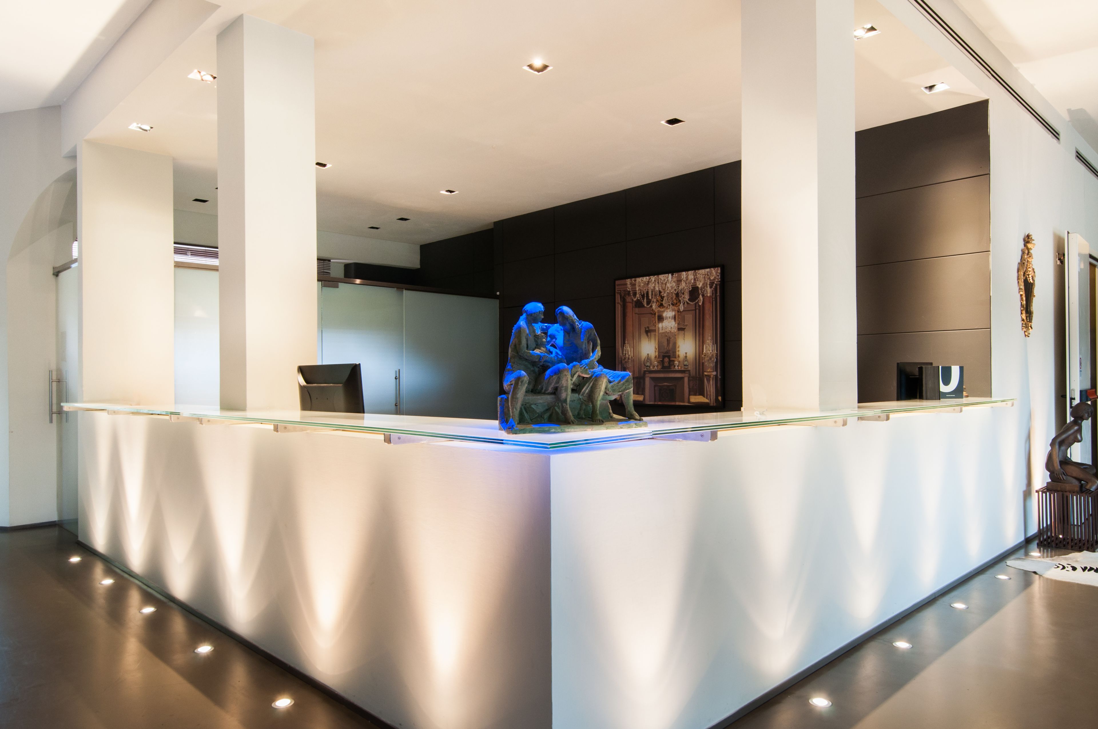 A modern reception area with a glass counter, a sculpture, and a chandelier.