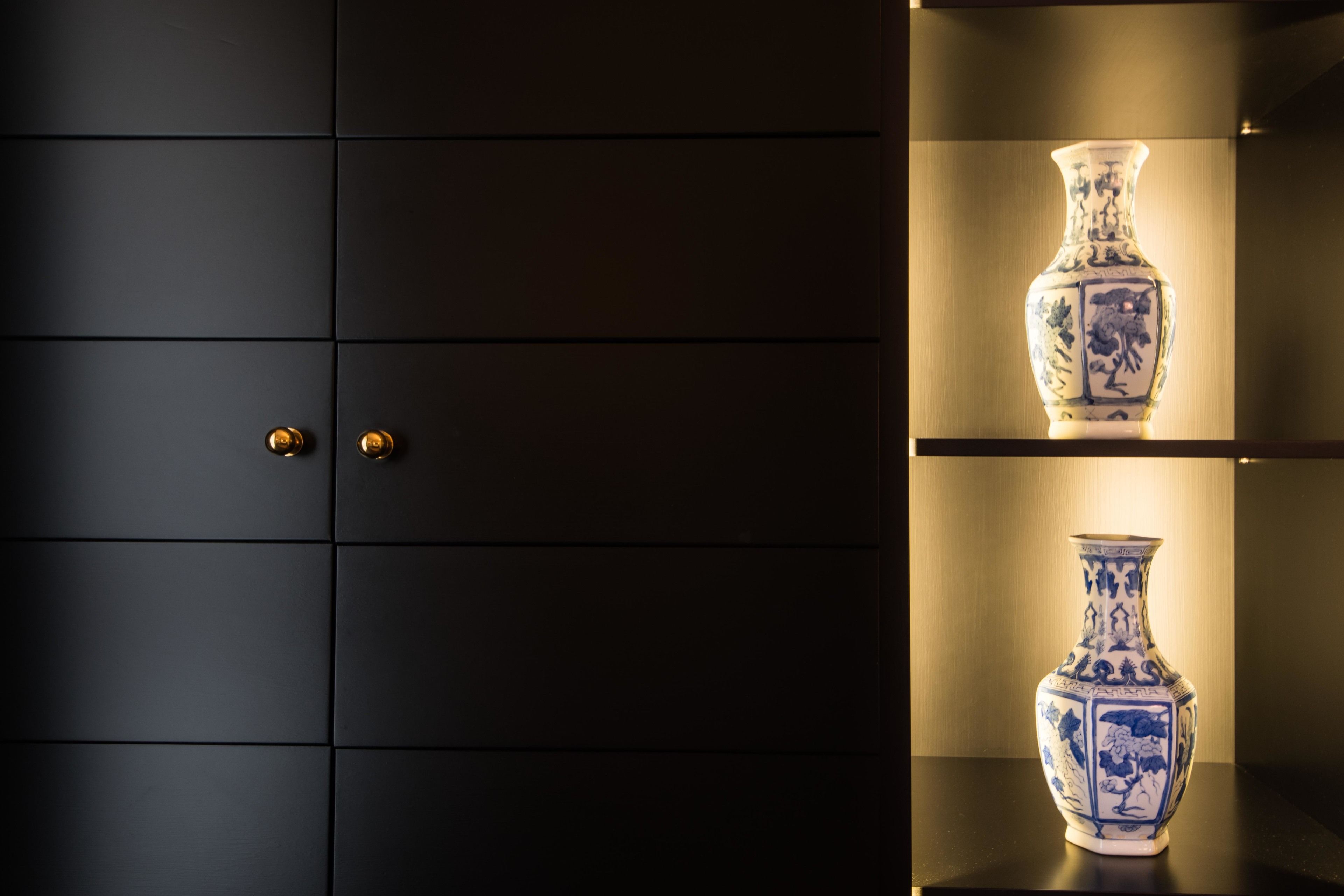 A dark room with two illuminated shelves displaying blue and white vases.