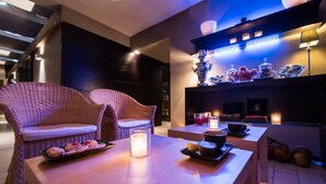 Un área de descanso moderna con sillones de mimbre, una mesa de madera con una vela y un estante con adornos.