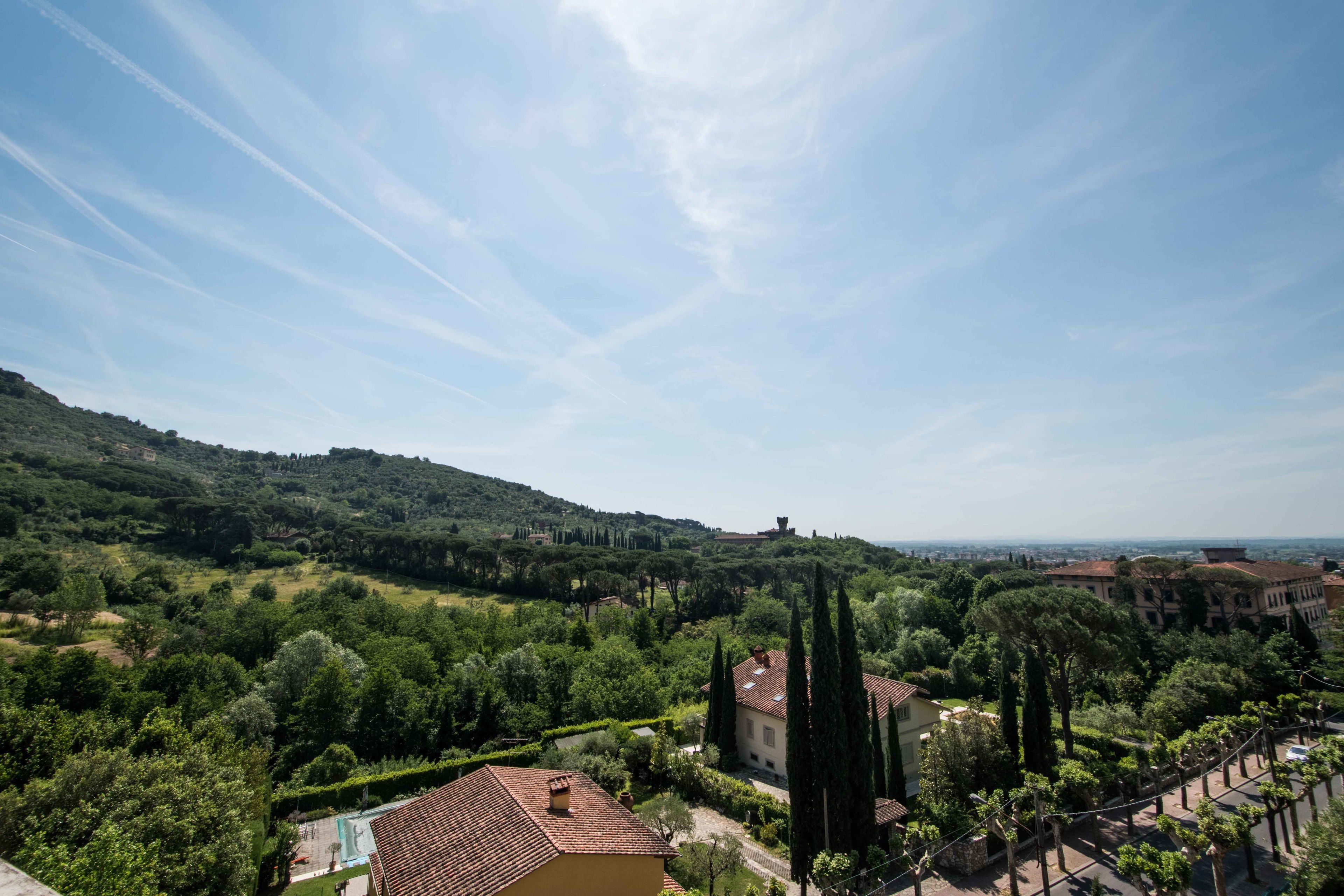 Una villa circondata da verde lussureggiante e colline, con un cielo sereno.