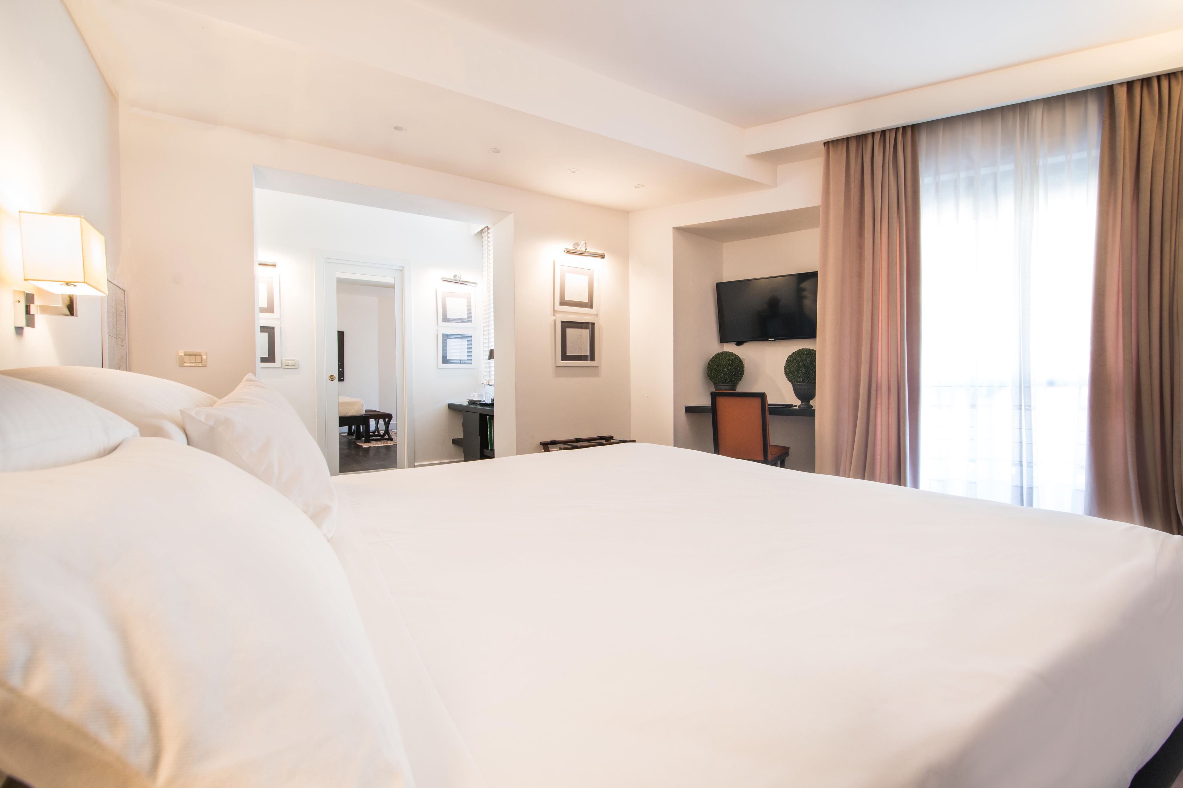 A hotel room with a large bed, a television mounted on the wall, and a desk with a chair.