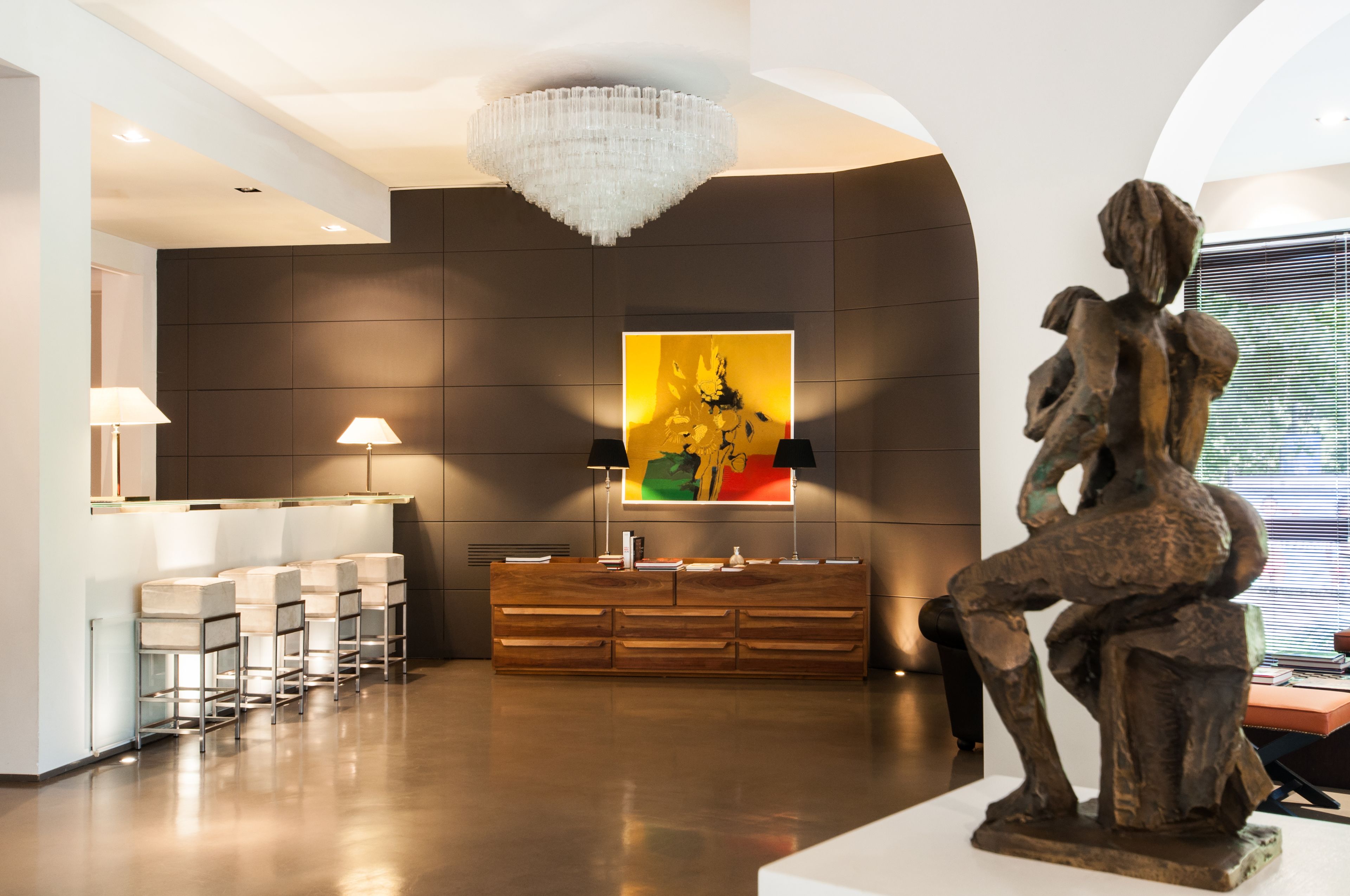 A modern lobby with a wooden reception desk, bar stools, a chandelier, and a large abstract painting.