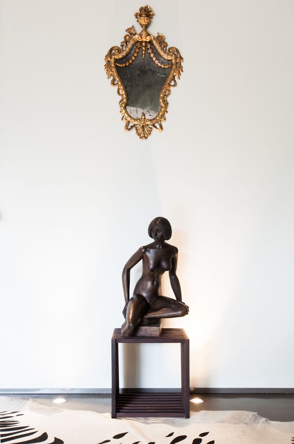 A sculpture of a seated figure on a pedestal against a plain wall, with a decorative mirror above it. - Hotel Michelangelo & Spa (Montecatini Terme)