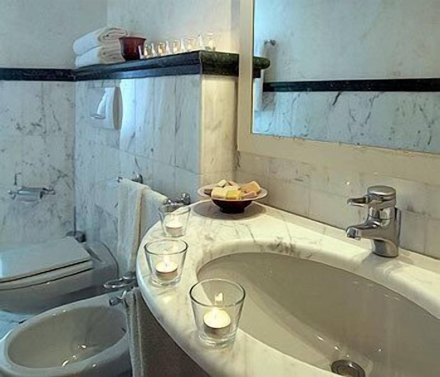 Un baño con un lavabo de mármol, un espejo, un inodoro y un pequeño recipiente con artículos de aseo en la encimera.