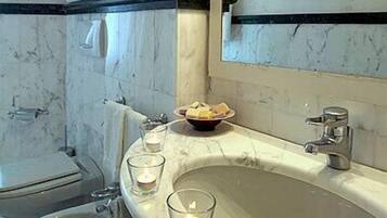 Un baño con un lavabo de mármol, un espejo, un inodoro y un pequeño recipiente con artículos de aseo en la encimera.