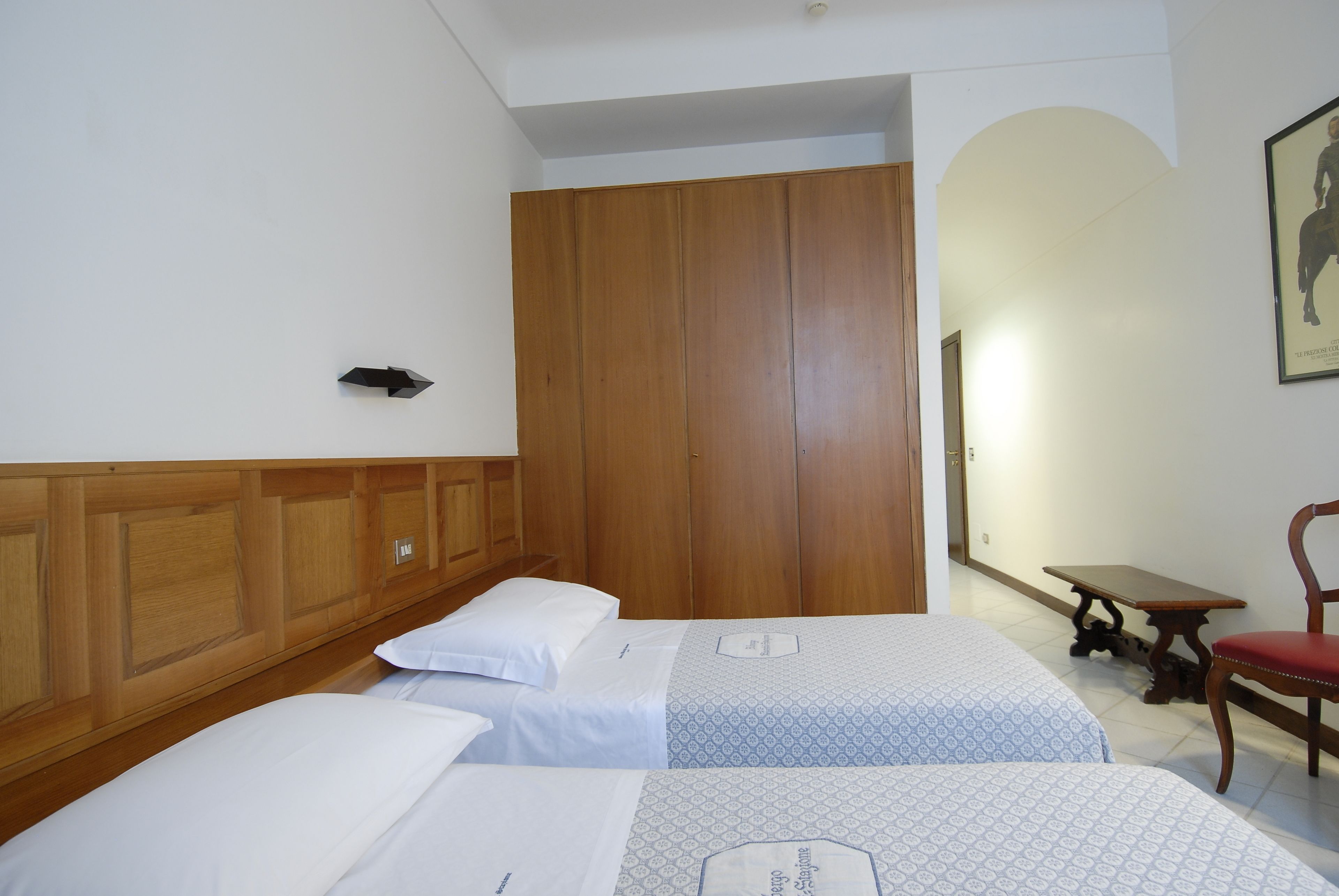 A hotel room with two beds, wooden wardrobe, a small table, and a chair.