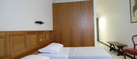 A hotel room with two beds, wooden wardrobe, a small table, and a chair.