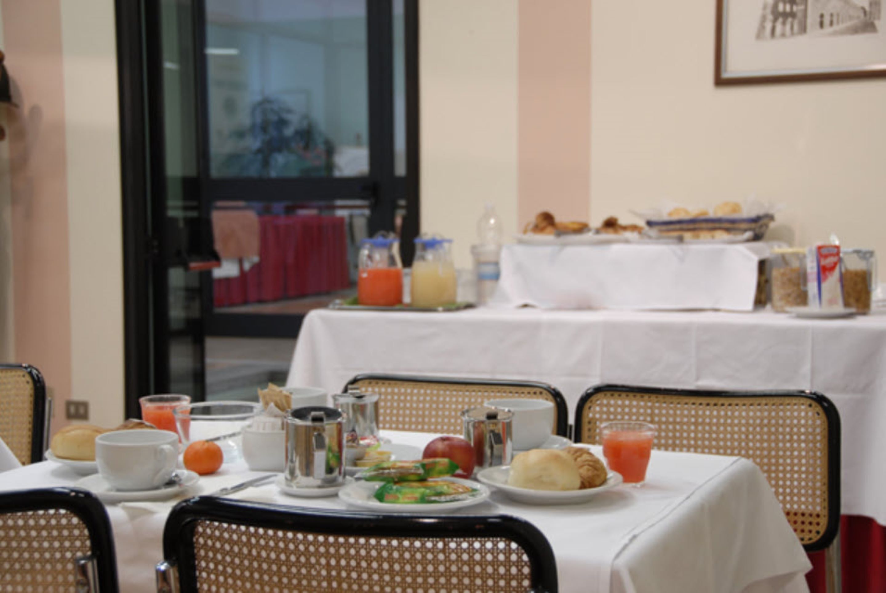 Une table mise pour le petit-déjeuner, avec une nappe, de la vaisselle, des boissons et un panier de viennoiseries.