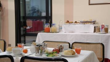Une table mise pour le petit-déjeuner, avec une nappe, de la vaisselle, des boissons et un panier de viennoiseries.
