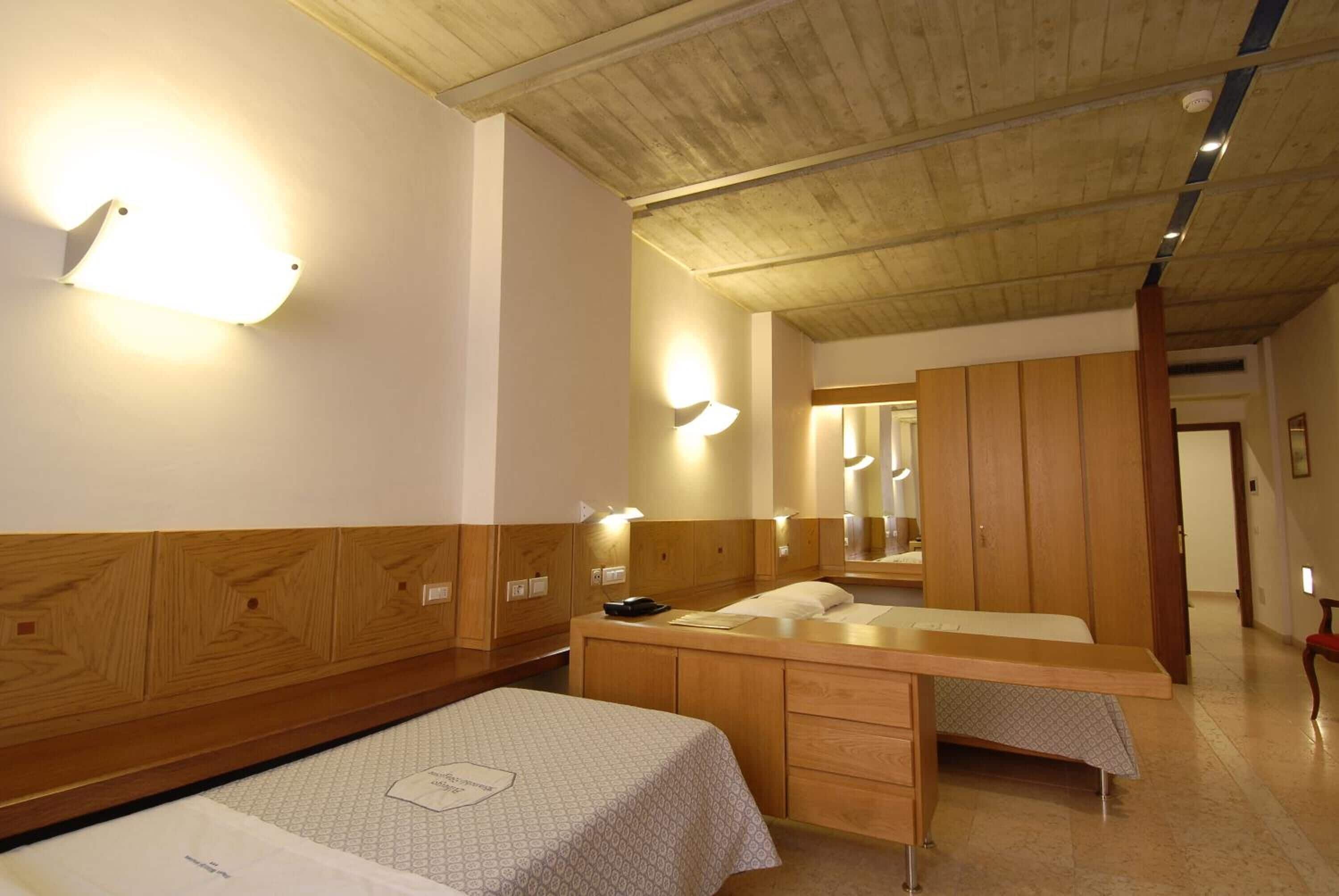 A hotel room with a wooden headboard, a bed with a patterned bedspread, a wooden dresser, and a mirror above the dresser.