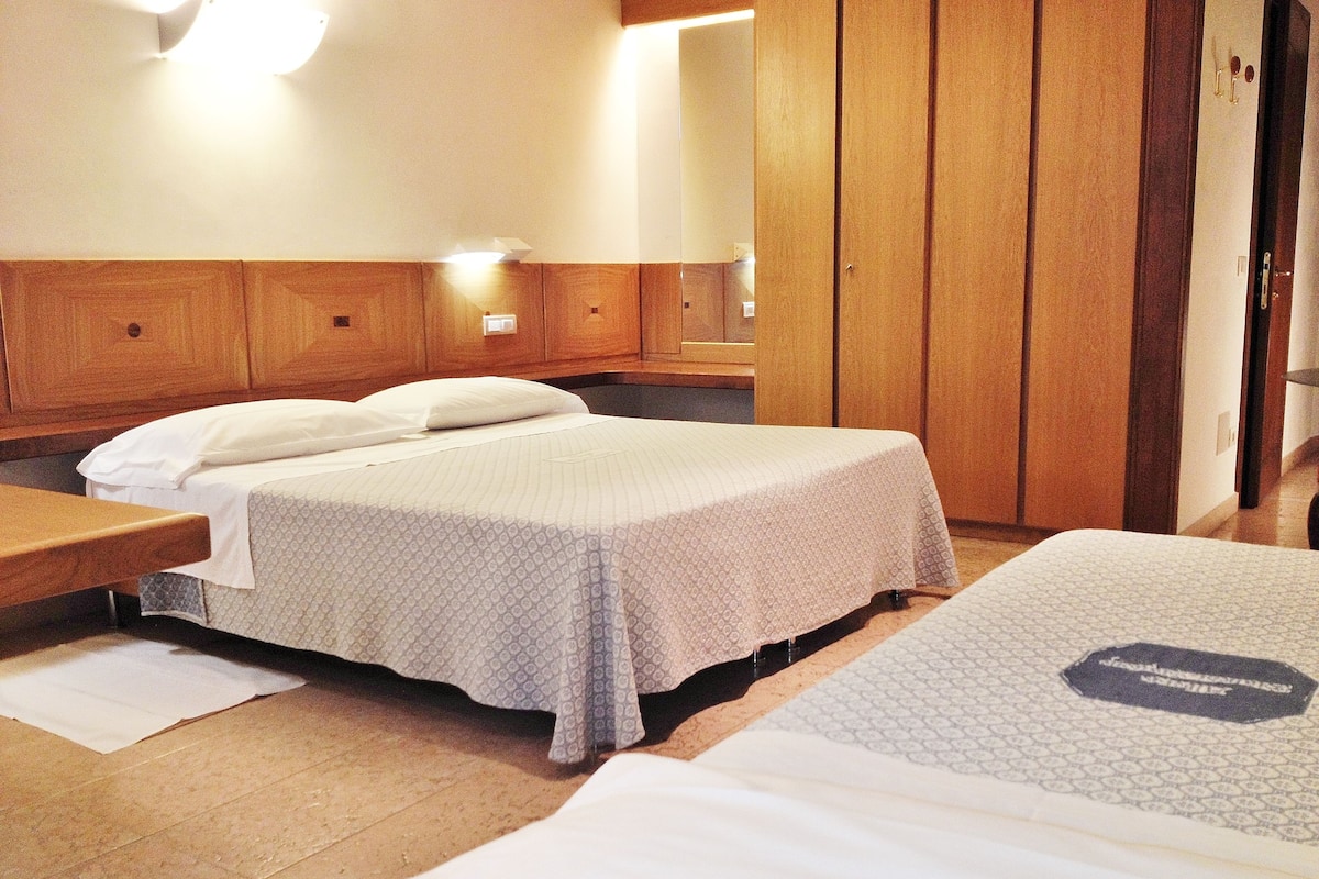 A hotel room with two beds, wooden headboards, and a wooden wardrobe.