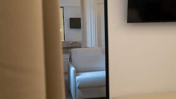 Una habitación de hotel con una cama, un banco, un televisor montado en la pared y una puerta que da a otra habitación.