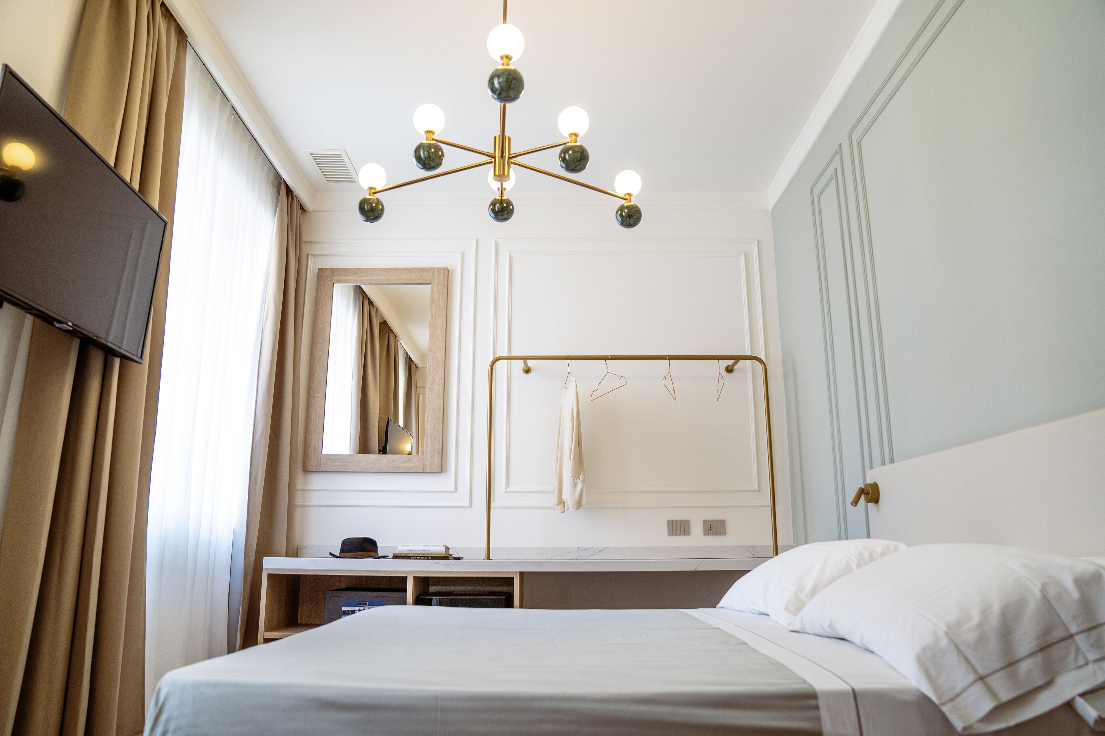 Una habitación de hotel con cama, escritorio, espejo y una araña.