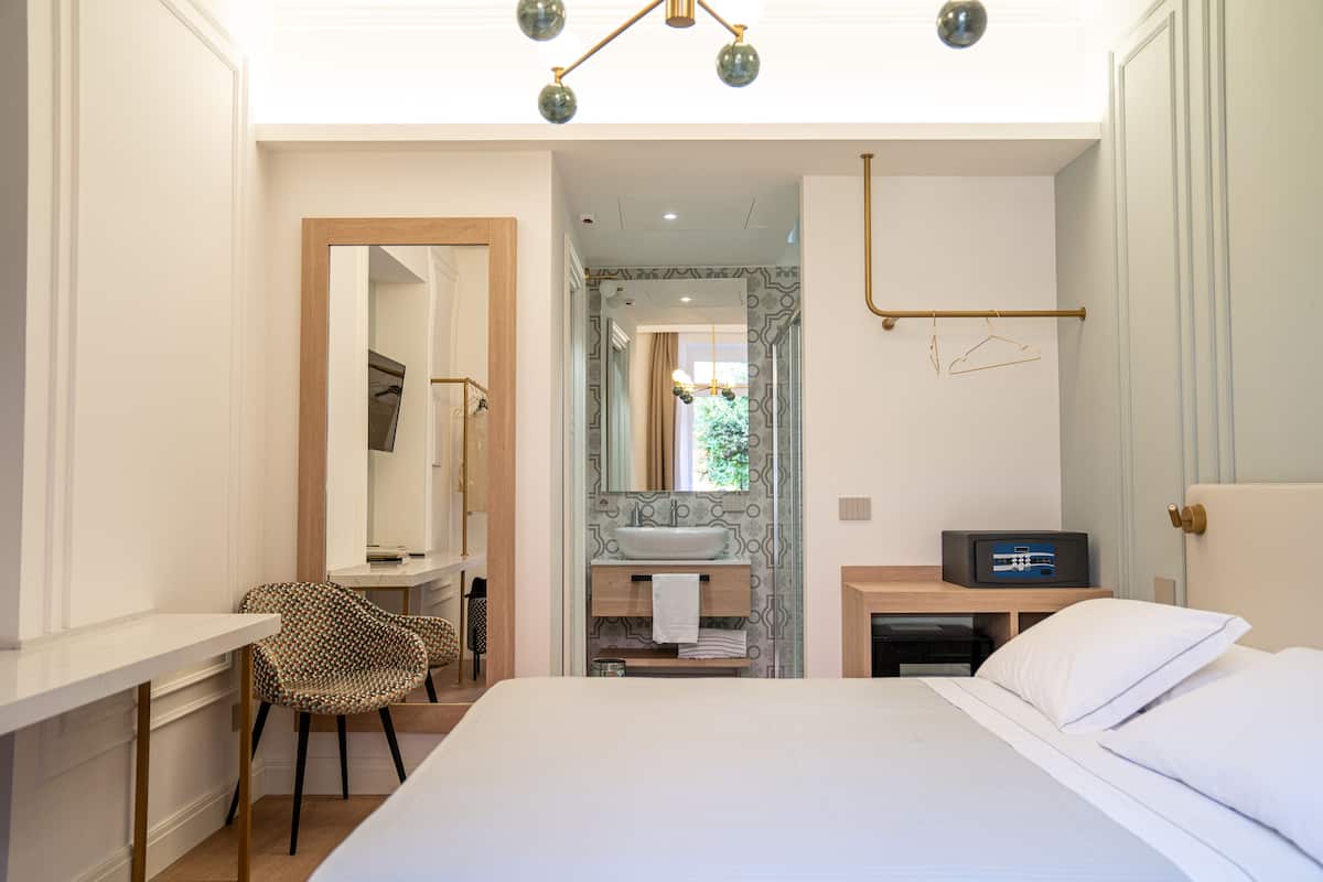 A modern hotel room with a large bed, a desk with a chair, a vanity with a mirror, and a bathroom with a sink and shower.