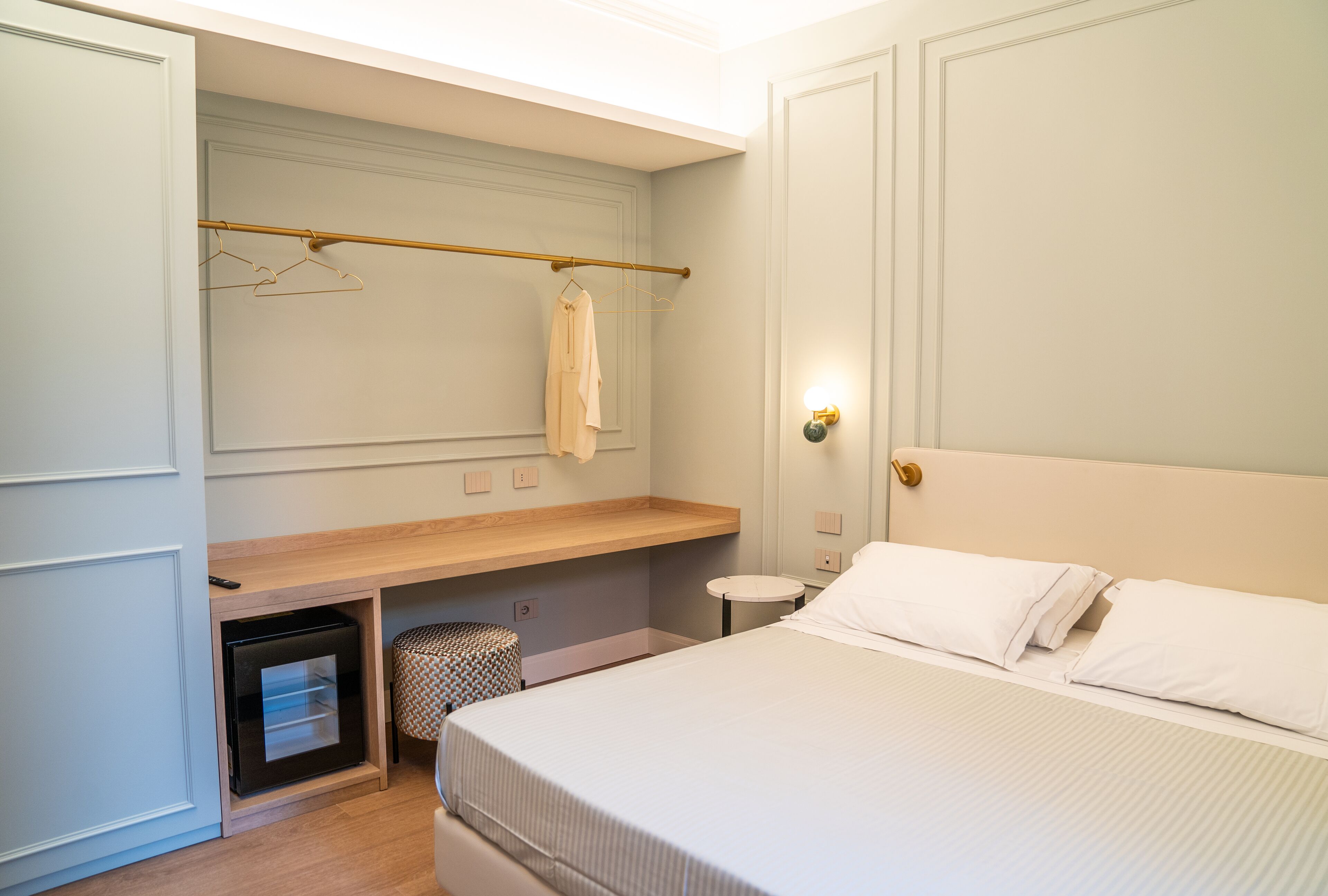 A bedroom with a bed, a bedside table, a wardrobe, and a hanging clothes rack.