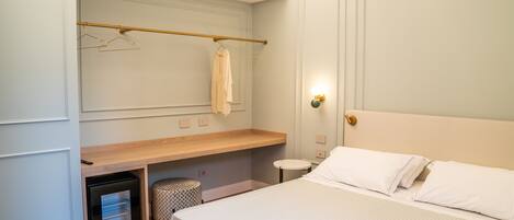 A bedroom with a bed, a bedside table, a wardrobe, and a hanging clothes rack.
