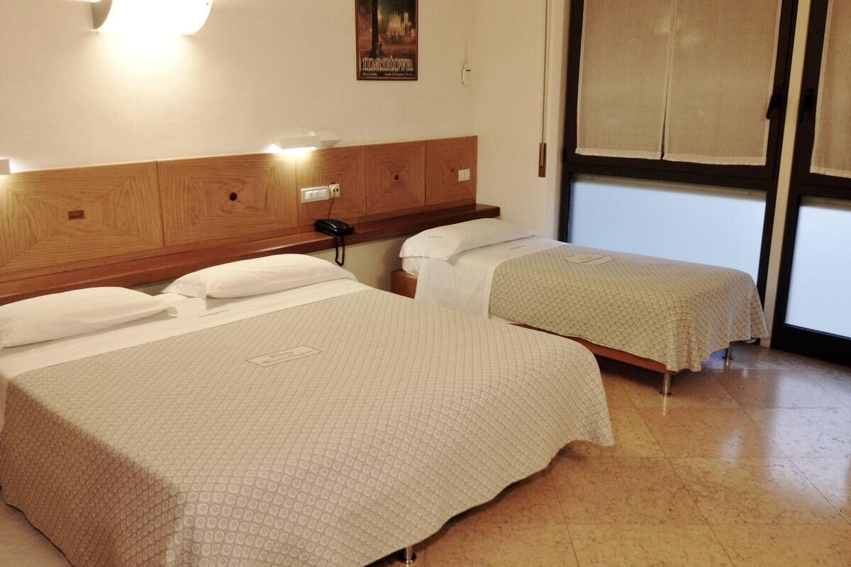 A hotel room with two beds, wooden headboard, bedside tables, a wall-mounted phone, and a poster.