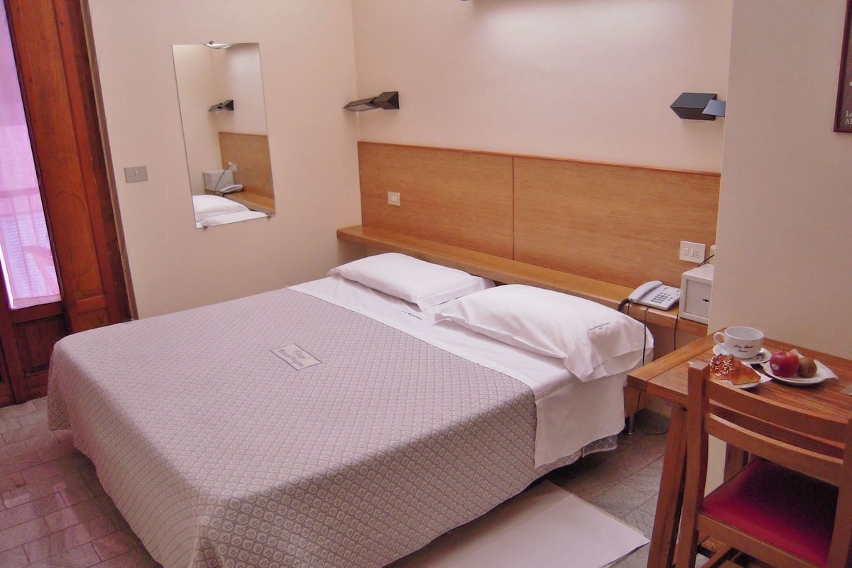 Una habitación de hotel con cama, mesita de noche y una silla.